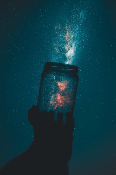 creative photo of person holding glass mason jar under a starry sky